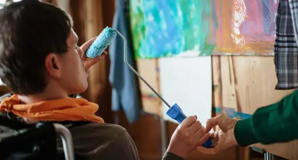 Bewohner im Rollstuhl mit Farbroller in der Hand am Bild malen