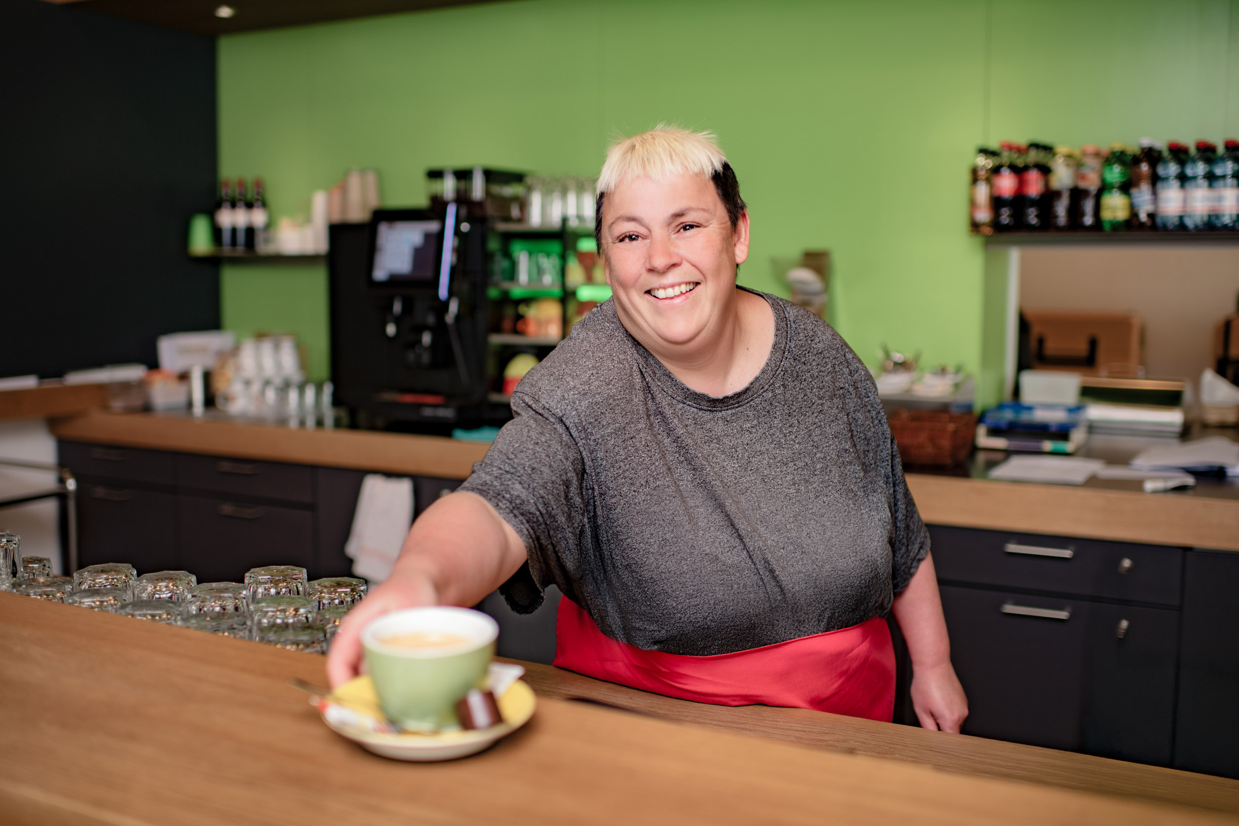 Frau hinter einer Theke die eine Tasse mit Kaffee entgegenstreckt